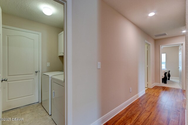 clothes washing area featuring visible vents, washer and dryer, baseboards, light wood-type flooring, and cabinet space