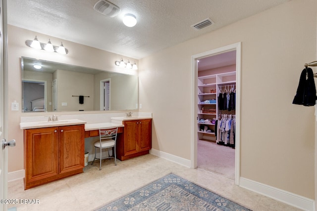 bathroom featuring visible vents, a sink, a spacious closet, and double vanity