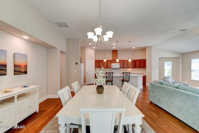 dining room featuring an inviting chandelier, baseboards, visible vents, and wood finished floors