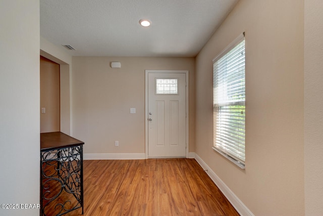 foyer with light wood finished floors, visible vents, baseboards, and a textured ceiling