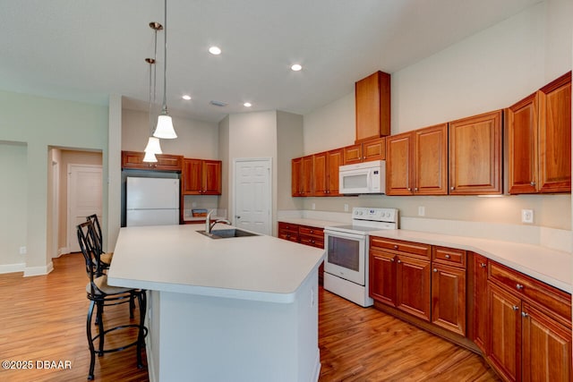 kitchen featuring a breakfast bar area, white appliances, a sink, and light wood finished floors