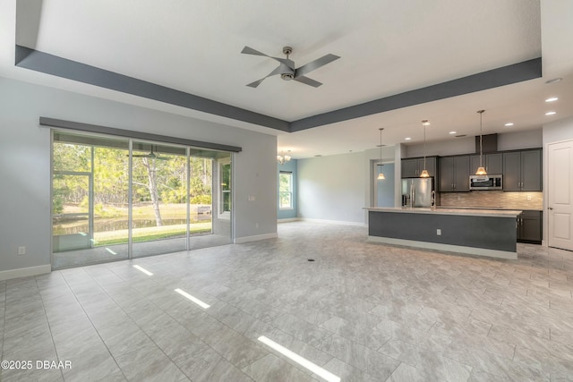 unfurnished living room featuring ceiling fan and a tray ceiling