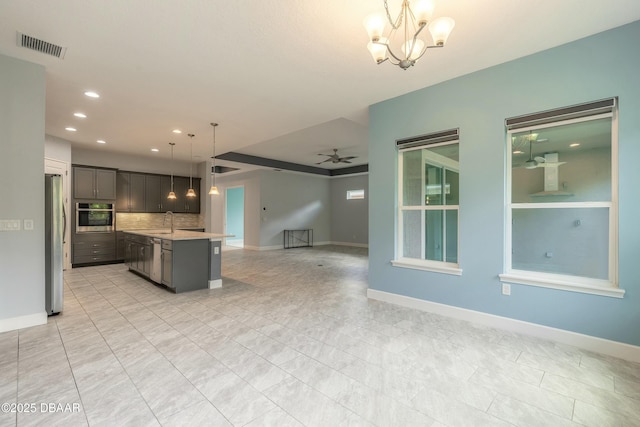 kitchen with sink, a kitchen island with sink, hanging light fixtures, stainless steel appliances, and ceiling fan with notable chandelier