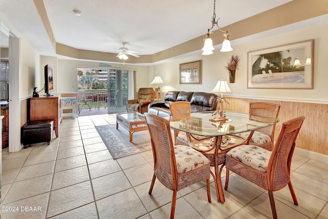 dining area featuring wood walls, light tile patterned floors, and ceiling fan with notable chandelier