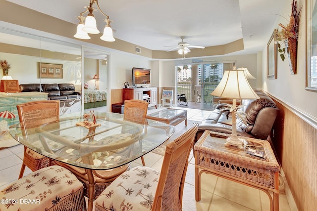 tiled dining space featuring wood walls, ceiling fan with notable chandelier, and a fireplace