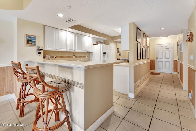 kitchen with kitchen peninsula, light tile patterned floors, a textured ceiling, white refrigerator with ice dispenser, and white cabinetry