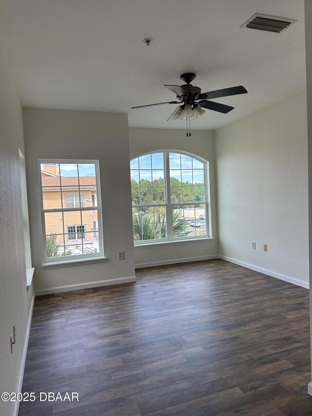 empty room with dark wood-type flooring, ceiling fan, and a wealth of natural light