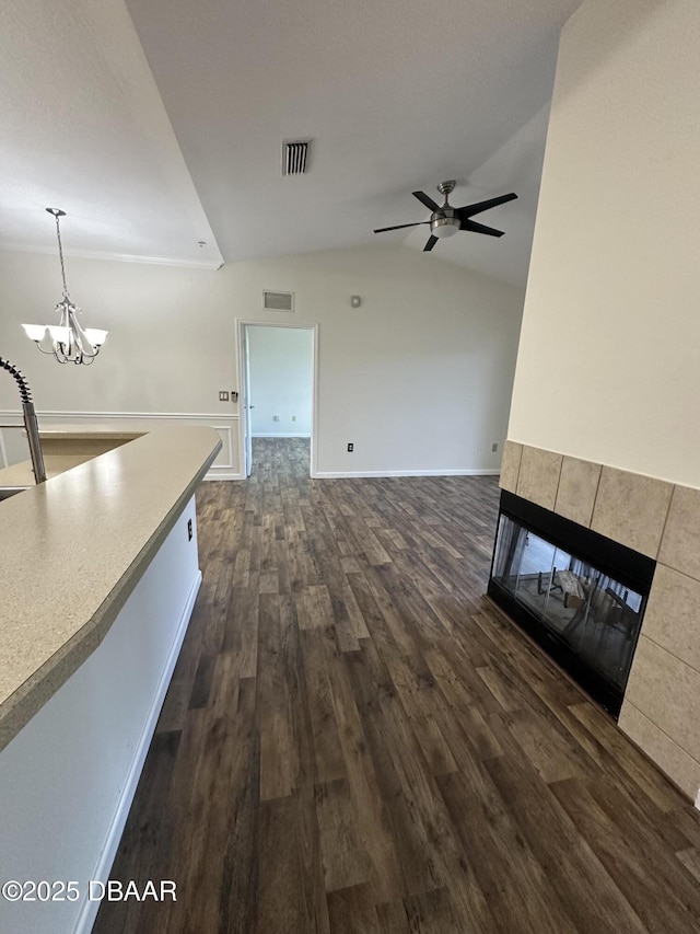 unfurnished living room featuring dark wood-type flooring, lofted ceiling, a fireplace, and ceiling fan with notable chandelier