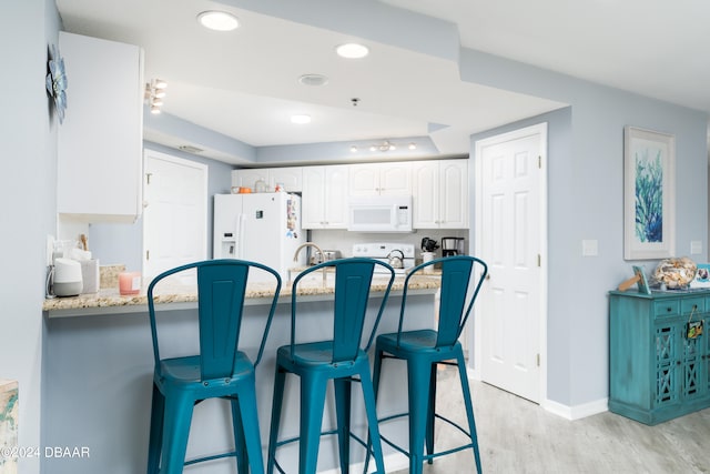 kitchen with white cabinets, a breakfast bar, light stone countertops, light wood-type flooring, and white appliances