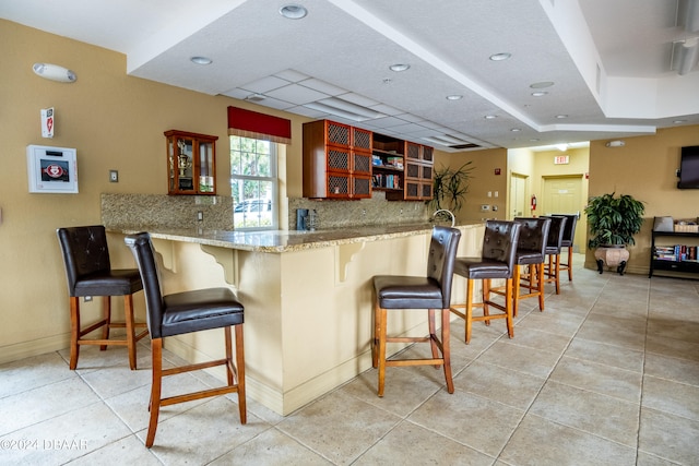 kitchen featuring kitchen peninsula, light tile patterned flooring, tasteful backsplash, and a breakfast bar