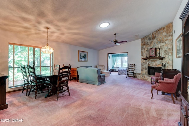 carpeted dining room featuring lofted ceiling, a textured ceiling, ceiling fan, and a stone fireplace