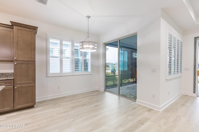 unfurnished dining area with an inviting chandelier, a wealth of natural light, and light wood-type flooring