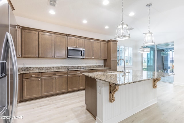 kitchen with sink, a kitchen breakfast bar, pendant lighting, stainless steel appliances, and a kitchen island with sink