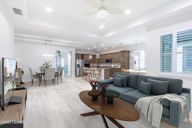 living room with light hardwood / wood-style flooring, ceiling fan, and a tray ceiling