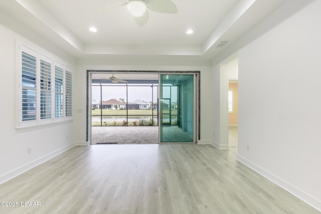 spare room with a tray ceiling, ceiling fan, and light wood-type flooring