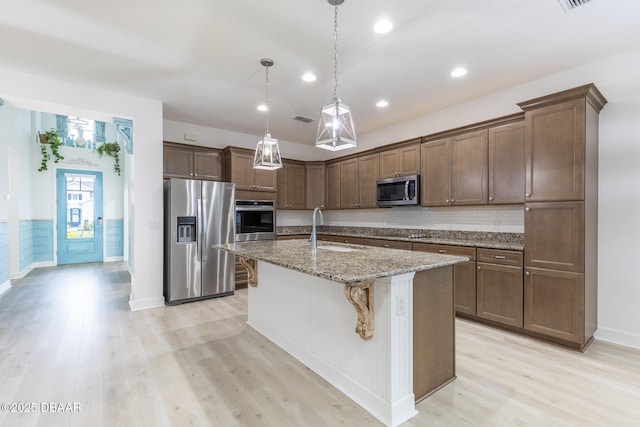 kitchen with pendant lighting, sink, a kitchen island with sink, stainless steel appliances, and light stone countertops