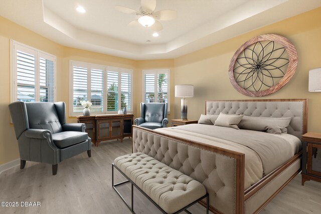 bedroom with ceiling fan, a raised ceiling, and light wood-type flooring