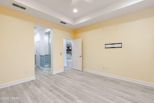 spare room featuring a raised ceiling, ceiling fan, and light hardwood / wood-style floors