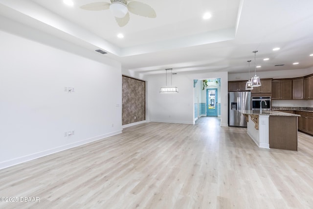 kitchen with appliances with stainless steel finishes, decorative light fixtures, a breakfast bar area, a kitchen island with sink, and light wood-type flooring