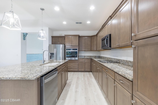 kitchen featuring stainless steel appliances, decorative light fixtures, sink, and a large island with sink