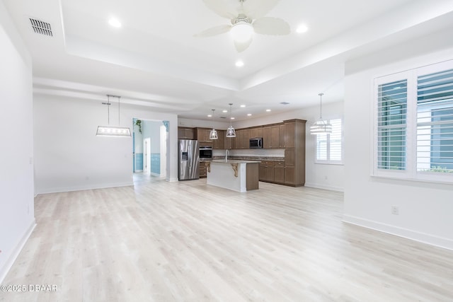 kitchen with a breakfast bar area, hanging light fixtures, appliances with stainless steel finishes, a tray ceiling, and a kitchen island