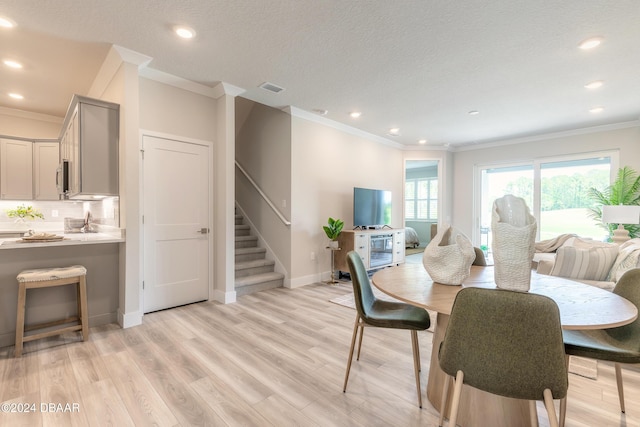 dining room with a textured ceiling, light wood-type flooring, and crown molding