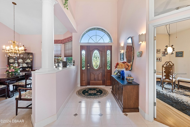 tiled entrance foyer featuring a notable chandelier, high vaulted ceiling, and decorative columns