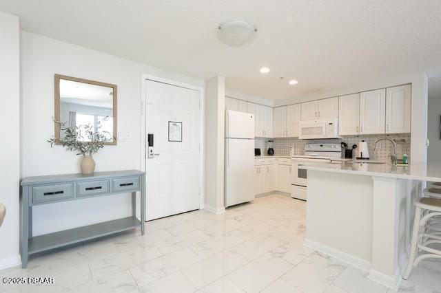 kitchen featuring marble finish floor, light countertops, backsplash, white appliances, and a peninsula