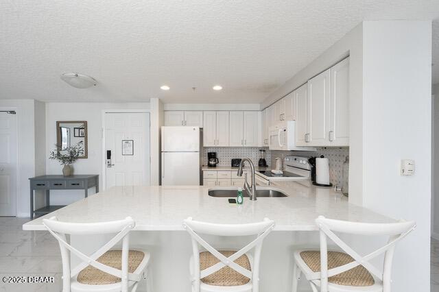 kitchen featuring backsplash, white cabinetry, a sink, white appliances, and a peninsula