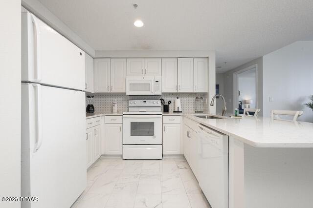 kitchen with white appliances, a peninsula, marble finish floor, light countertops, and a sink