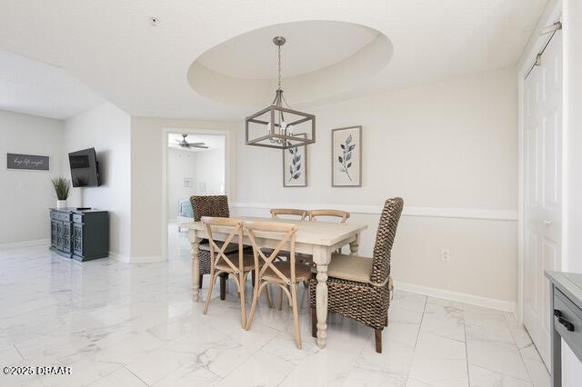 dining room featuring marble finish floor, baseboards, a tray ceiling, and a ceiling fan