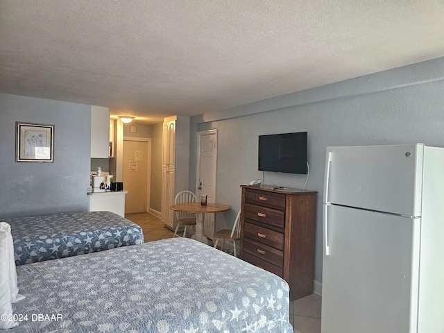 tiled bedroom with a textured ceiling and white fridge