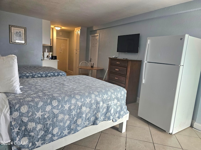 bedroom featuring a textured ceiling, light tile patterned floors, and white fridge