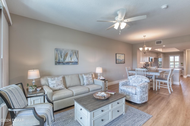 living room featuring ceiling fan with notable chandelier, light hardwood / wood-style floors, and a textured ceiling