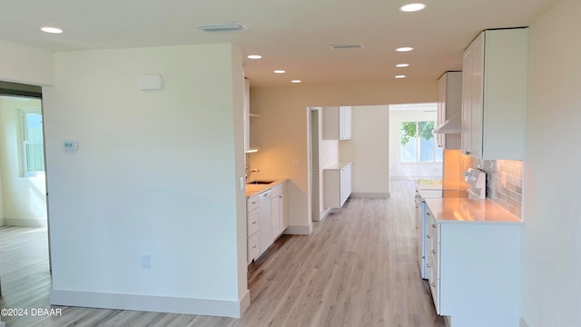 kitchen featuring white appliances, radiator heating unit, range hood, white cabinets, and light wood-type flooring