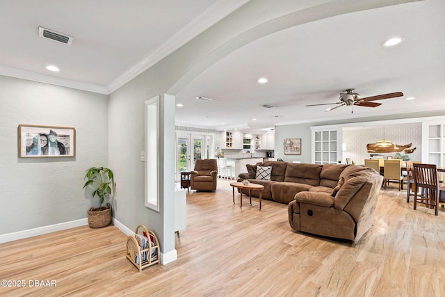 living room with arched walkways, visible vents, ornamental molding, light wood-style floors, and baseboards