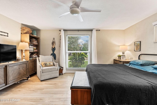 bedroom with a ceiling fan, a textured wall, a textured ceiling, and light wood finished floors