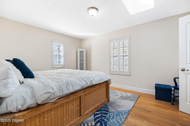 bedroom with hardwood / wood-style floors, a textured ceiling, and a skylight