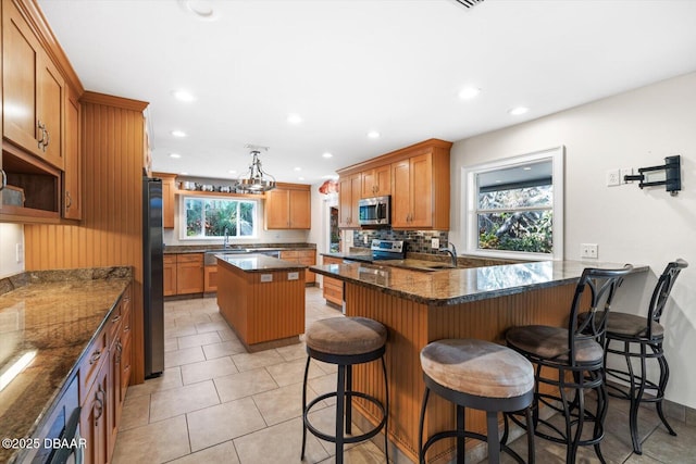 kitchen featuring appliances with stainless steel finishes, a kitchen bar, decorative backsplash, dark stone counters, and a center island