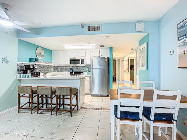 kitchen featuring light tile patterned flooring, appliances with stainless steel finishes, decorative backsplash, white cabinets, and kitchen peninsula