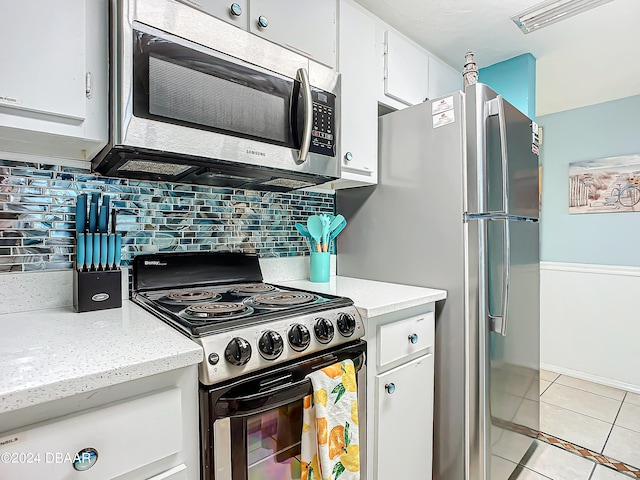 kitchen featuring stainless steel appliances, light stone counters, light tile patterned floors, tasteful backsplash, and white cabinetry