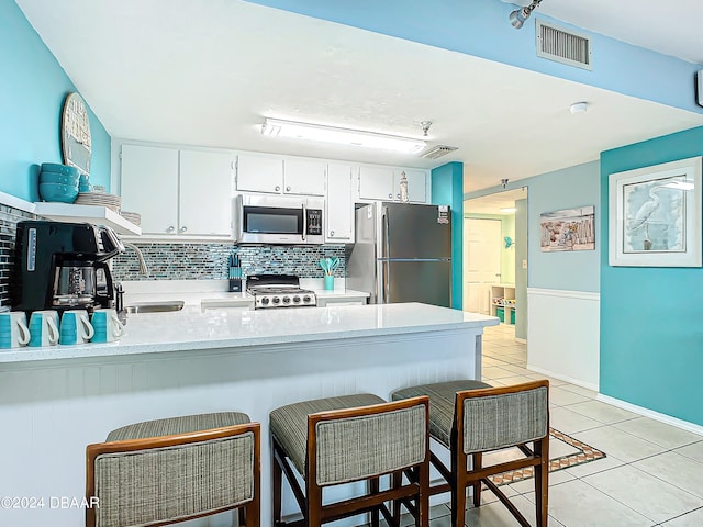 kitchen featuring stainless steel appliances, light tile patterned flooring, white cabinetry, kitchen peninsula, and decorative backsplash