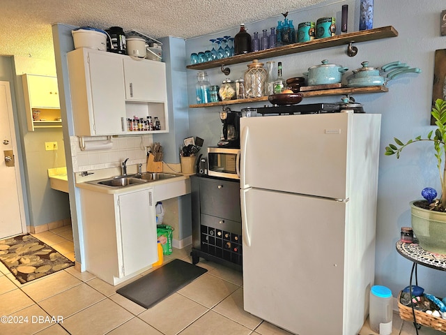 kitchen featuring white cabinetry, sink, white refrigerator, a textured ceiling, and light tile patterned floors