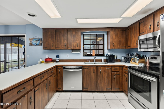 kitchen featuring dark brown cabinetry, light tile patterned flooring, sink, kitchen peninsula, and appliances with stainless steel finishes