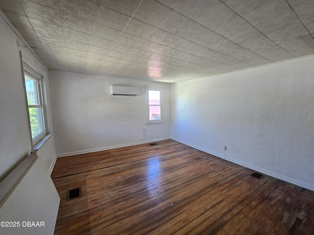 spare room with a wall unit AC, visible vents, baseboards, and hardwood / wood-style flooring