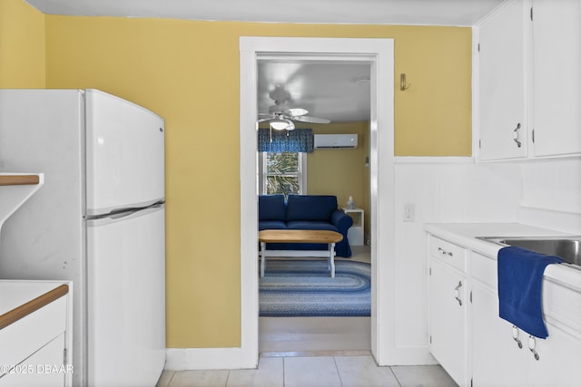 kitchen featuring light tile patterned flooring, a wall unit AC, white fridge, and white cabinets