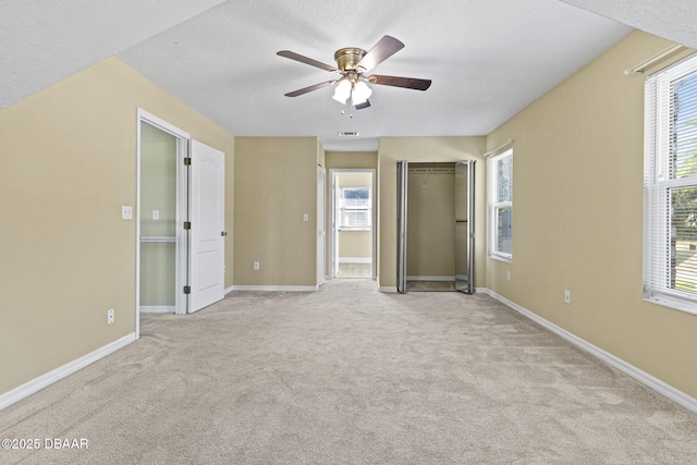 unfurnished bedroom featuring light carpet, ceiling fan, a textured ceiling, and baseboards