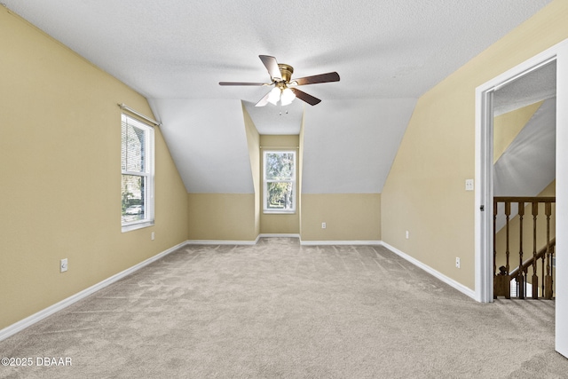 bonus room featuring lofted ceiling, baseboards, a textured ceiling, and light colored carpet