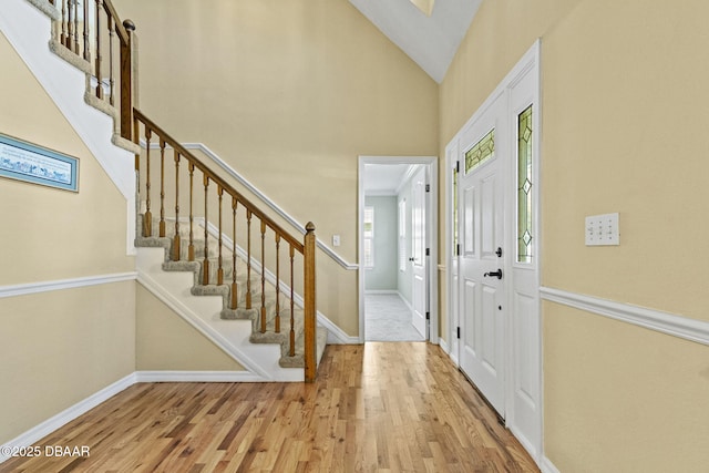 entryway featuring stairs, high vaulted ceiling, baseboards, and light wood-style floors