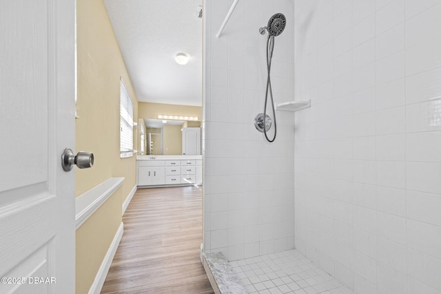 full bath featuring baseboards, tiled shower, wood finished floors, a textured ceiling, and vanity